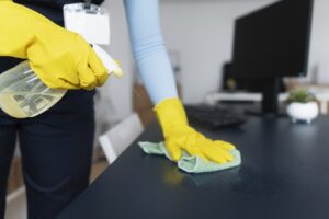 A lady cleaning a surface with gloves, rags and disinfecting spray
